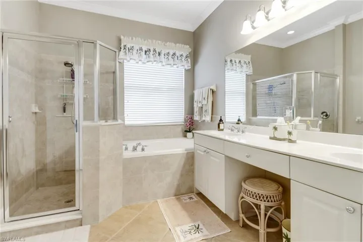 Full bathroom with double vanity, a stall shower, a garden tub, light tile patterned floors, and ornamental molding