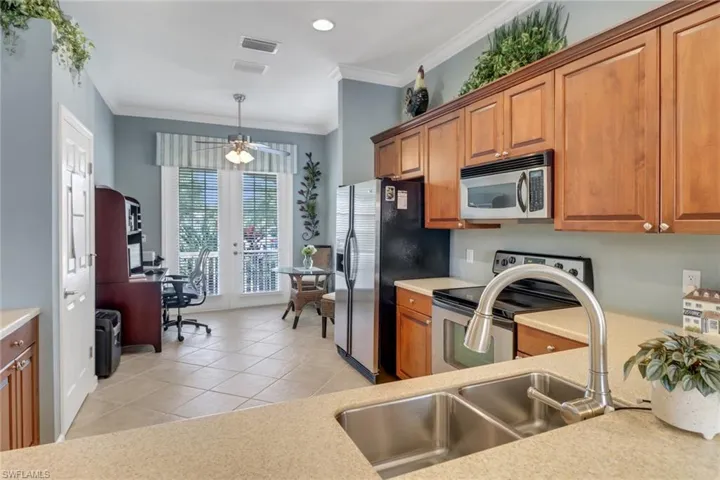 Kitchen featuring brown cabinets, stainless steel appliances, a desk, ornamental molding, and light tile patterned floors
