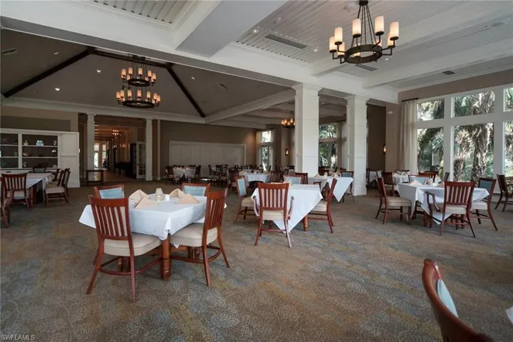 Carpeted dining space featuring a chandelier, beamed ceiling, ornate columns, ornamental molding, and a high ceiling