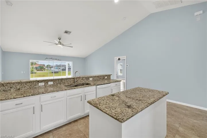 Kitchen featuring white cabinetry, light stone countertops, lofted ceiling, ceiling fan, and dishwasher
