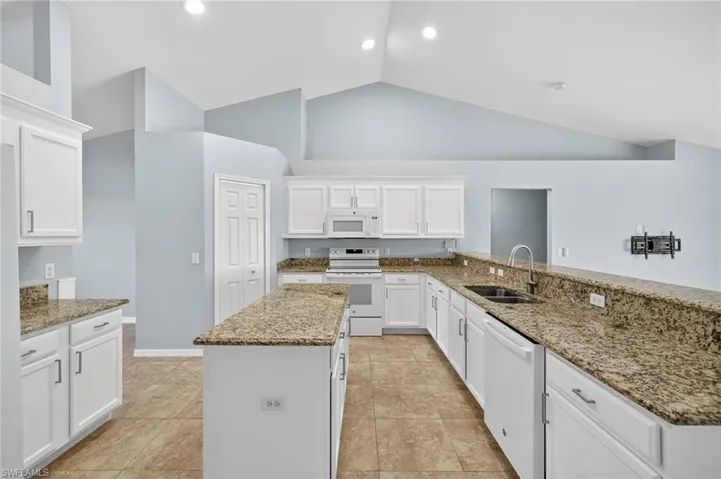 Kitchen featuring white cabinets, dark stone countertops, white appliances, a center island, and high vaulted ceiling