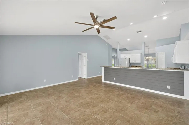Unfurnished living room with vaulted ceiling, ceiling fan, and light tile patterned flooring