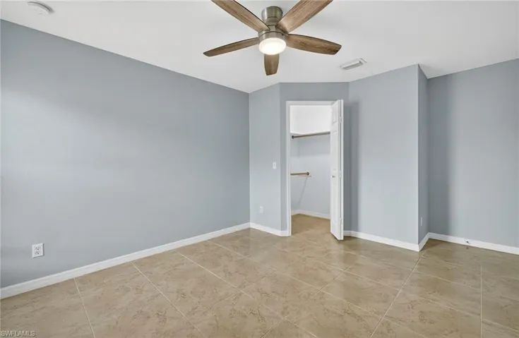 Unfurnished bedroom featuring a walk in closet, a ceiling fan, and light tile patterned floors