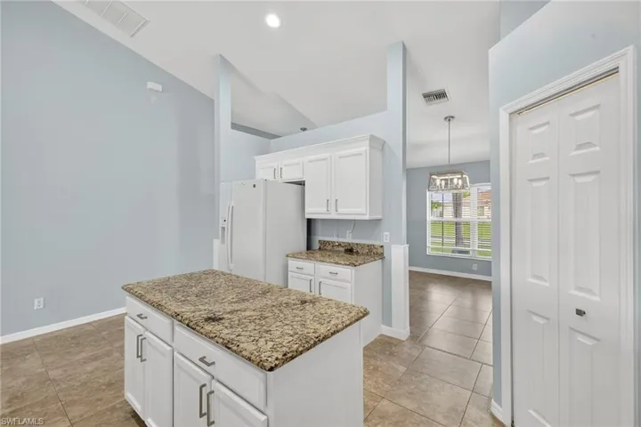 Kitchen featuring white refrigerator with ice dispenser, white cabinetry, a kitchen island, light tile patterned flooring, and light stone countertops