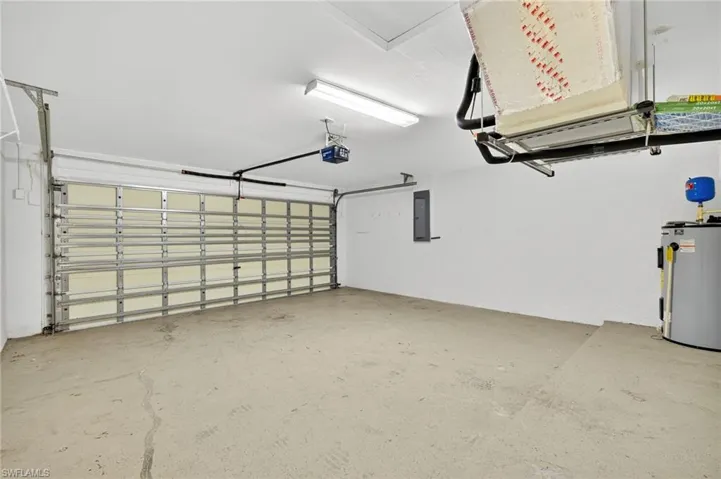 Garage with electric water heater, electric panel, and a garage door opener