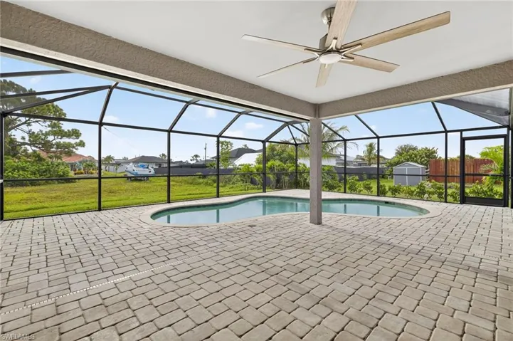 Swimming pool with screen enclosure, a patio, a sunroom, a yard, and a storage unit