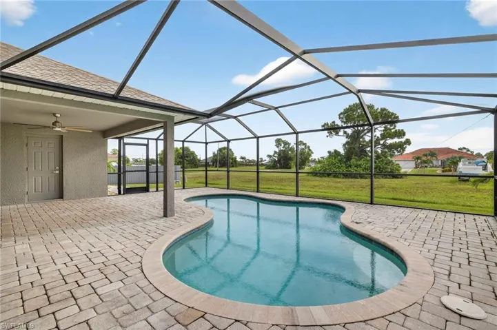 Outdoor pool with glass enclosure, a patio, a sunroom, a yard, and a ceiling fan