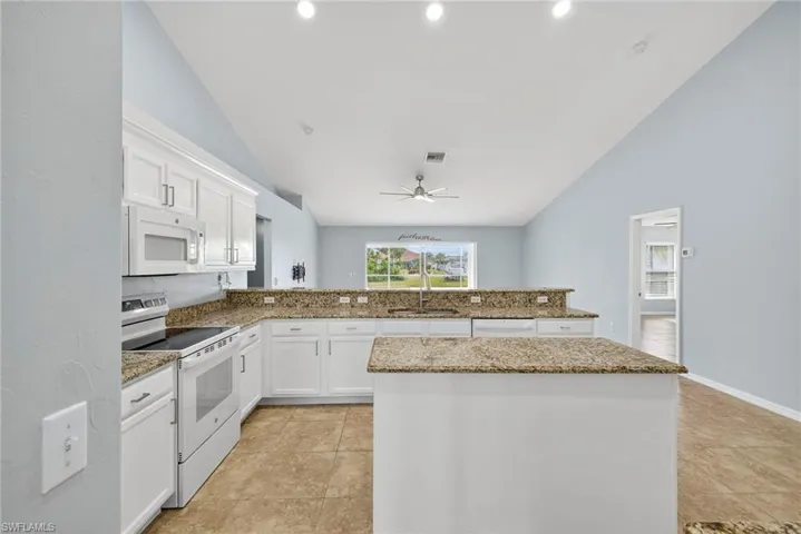 Kitchen with white cabinetry, white appliances, a peninsula, light stone counters, and high vaulted ceiling