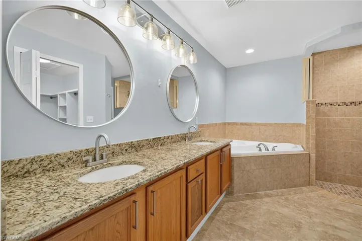 Bathroom featuring a garden tub, double vanity, light tile patterned floors, and recessed lighting