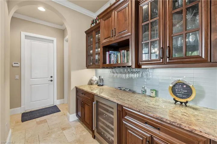 Bar with light stone countertops, tasteful backsplash, beverage cooler, and crown molding