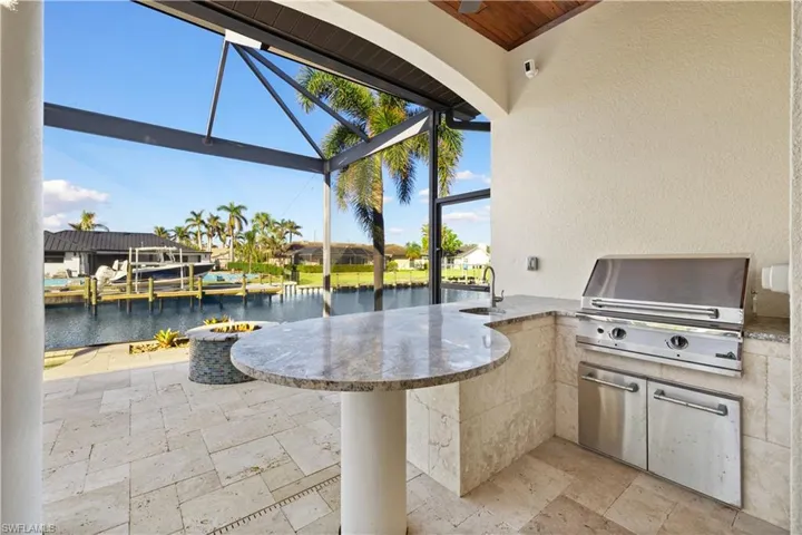 View of patio / terrace with a water view, an outdoor wet bar, grilling area, and a lanai