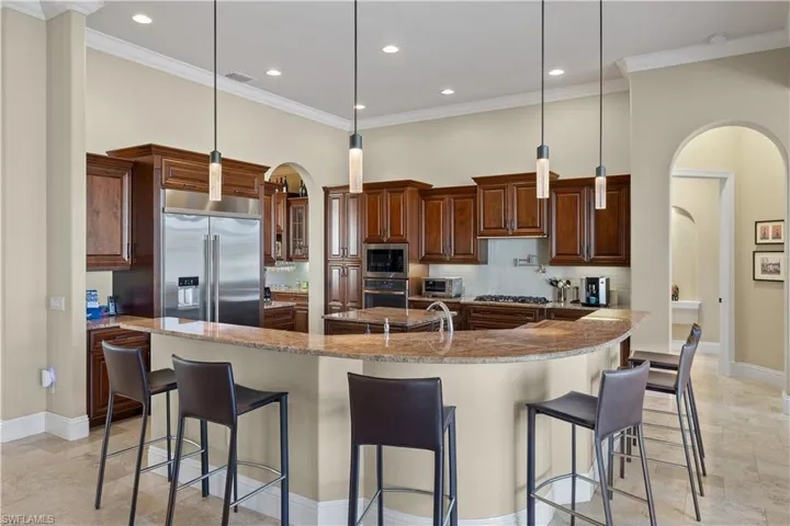 Kitchen with a large island, built in appliances, decorative light fixtures, a kitchen bar, and decorative backsplash