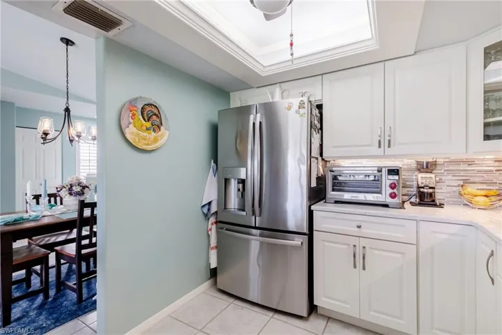 Kitchen with white cabinetry, stainless steel fridge with ice dispenser, light stone countertops, and light tile patterned floors