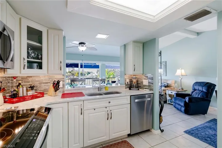 Kitchen featuring appliances with stainless steel finishes, white cabinets, glass insert cabinets, light stone countertops, and light tile patterned floors