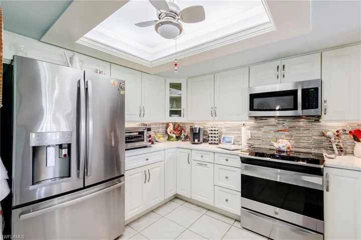 Kitchen with stainless steel appliances, a tray ceiling, light stone counters, crown molding, and white cabinetry