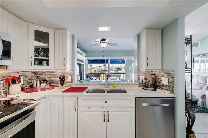 Kitchen featuring appliances with stainless steel finishes, white cabinets, light stone counters, and ceiling fan