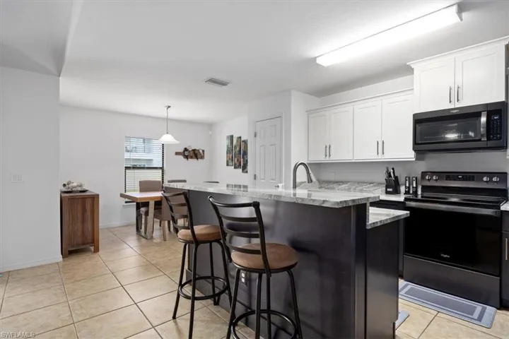 Kitchen with electric range, light tile patterned floors, a kitchen bar, white cabinetry, and pendant lighting