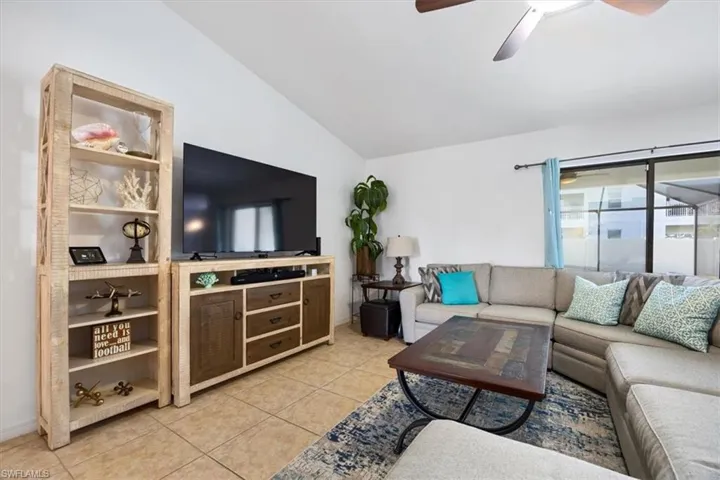 Living room featuring vaulted ceiling, a ceiling fan, and light tile patterned floors
