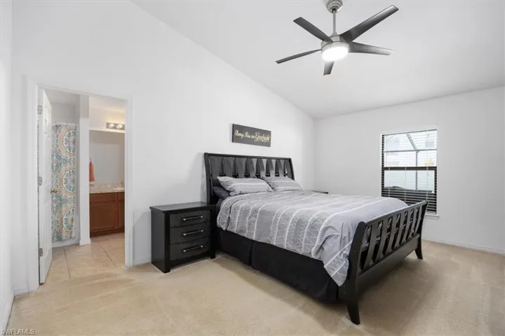 Bedroom featuring vaulted ceiling, ensuite bathroom, light colored carpet, and ceiling fan