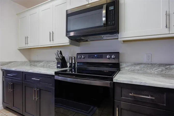 Kitchen featuring electric stove, stainless steel microwave, white cabinets, light stone counters, and light tile patterned floors