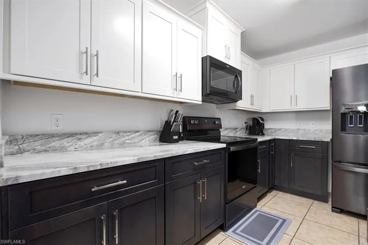 Kitchen featuring black appliances, white cabinetry, dark cabinetry, light tile patterned flooring, and light stone counters