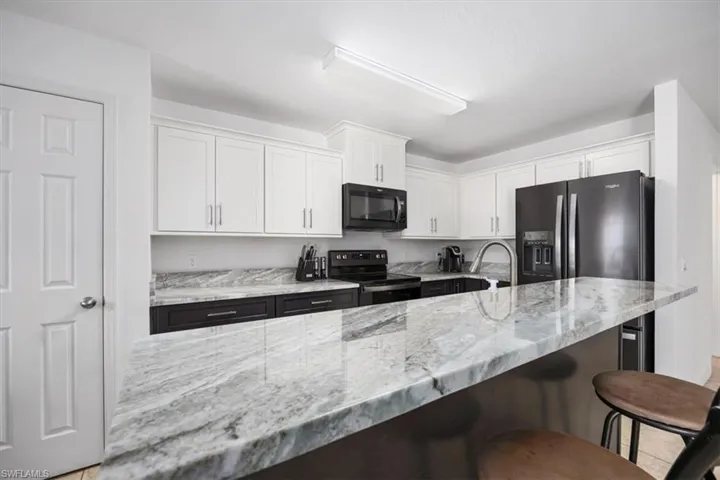 Kitchen with white cabinetry, light stone counters, a kitchen breakfast bar, and black appliances
