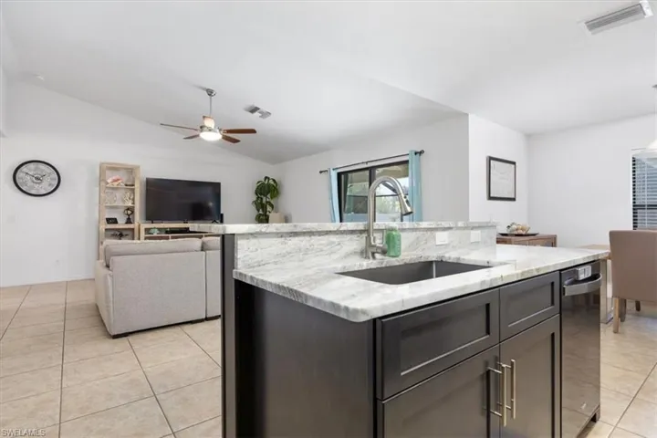 Kitchen with light tile patterned flooring, a center island with sink, vaulted ceiling, light stone counters, and open floor plan