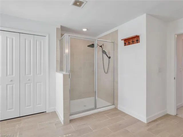 Bathroom with a closet, wood finish floors, a shower stall, and recessed lighting