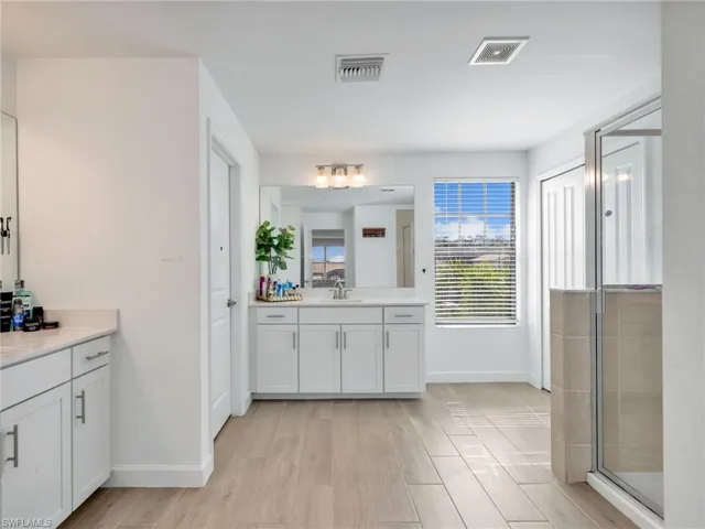 Full bathroom featuring light wood finished floors, two vanities, and a stall shower