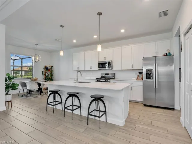Kitchen with stainless steel appliances, white cabinetry, hanging light fixtures, and wood finish floors