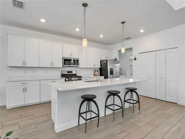 Kitchen featuring stainless steel appliances, wood finish floors, white cabinetry, a center island with sink, and a kitchen bar