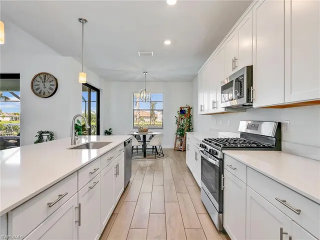 Kitchen with stainless steel appliances, white cabinetry, wood tiled floors, pendant lighting, and light stone counters