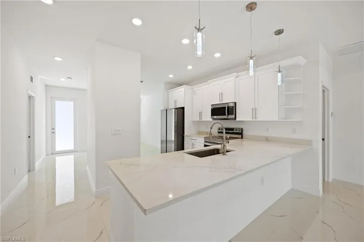Kitchen featuring hanging light fixtures, light stone counters, kitchen peninsula, white cabinets, and appliances with stainless steel finishes