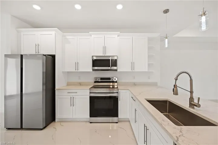 Kitchen with light stone countertops, stainless steel appliances, sink, decorative light fixtures, and white cabinets