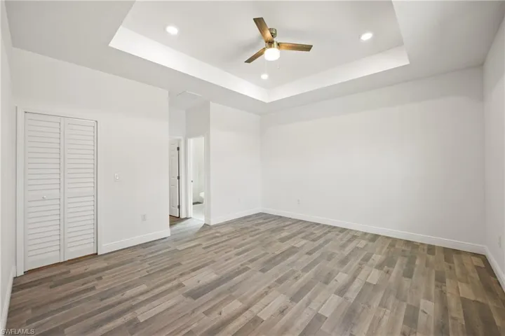 Unfurnished bedroom featuring a closet, a tray ceiling, ceiling fan, and dark wood-type flooring