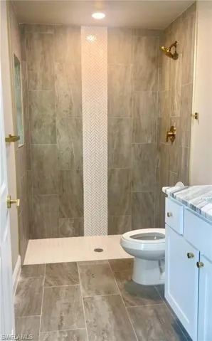 Bathroom with tile floors, a tile shower, tile walls, vanity, and toilet