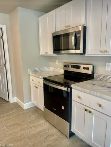 Kitchen with light stone countertops, stainless steel appliances, and white cabinetry