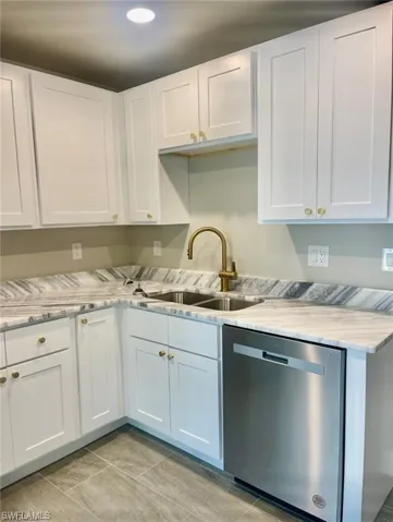 Kitchen featuring sink, white cabinetry, stainless steel dishwasher, and light tile floors