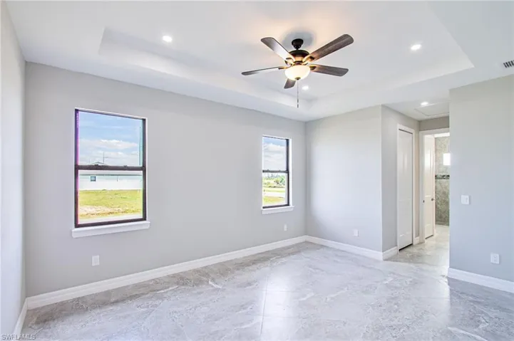 Unfurnished room featuring a tray ceiling, ceiling fan, and light tile patterned floors