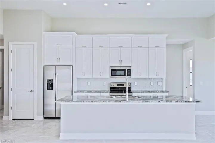 Kitchen with stainless steel appliances, white cabinetry, and a center island with sink