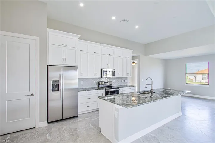 Kitchen with appliances with stainless steel finishes, white cabinets, an island with sink, and sink