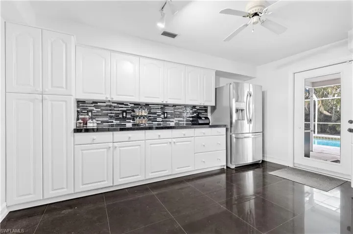 Kitchen with decorative backsplash, stainless steel fridge, ceiling fan, dark tile patterned flooring, and white cabinetry
