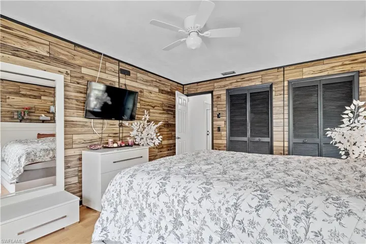 Bedroom featuring ceiling fan, light hardwood / wood-style flooring, two closets, and wooden walls