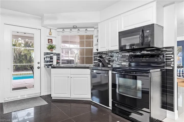 Kitchen featuring sink, dark tile patterned floors, decorative backsplash, white cabinets, and black appliances