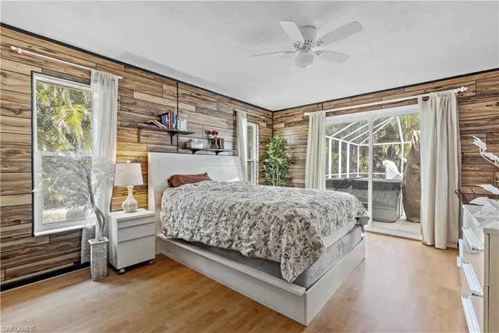 Bedroom featuring access to exterior, light hardwood / wood-style flooring, ceiling fan, and wooden walls