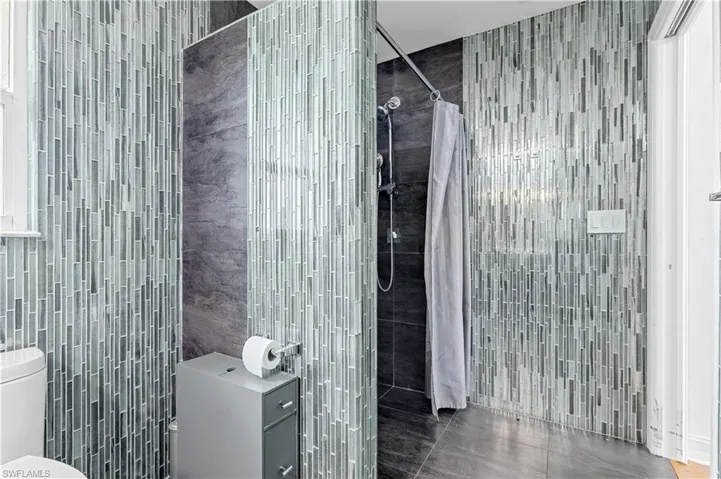 Bathroom featuring toilet, tile patterned flooring, tile walls, and walk in shower