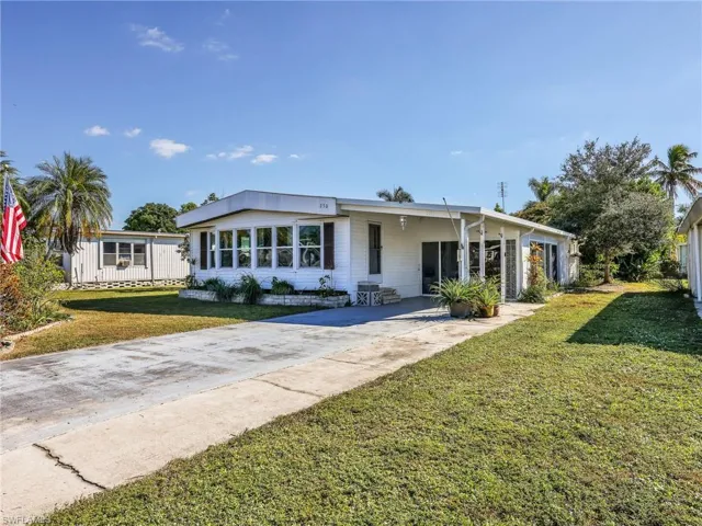 View of front of property with concrete driveway, a carport, a front lawn, and a sunroom