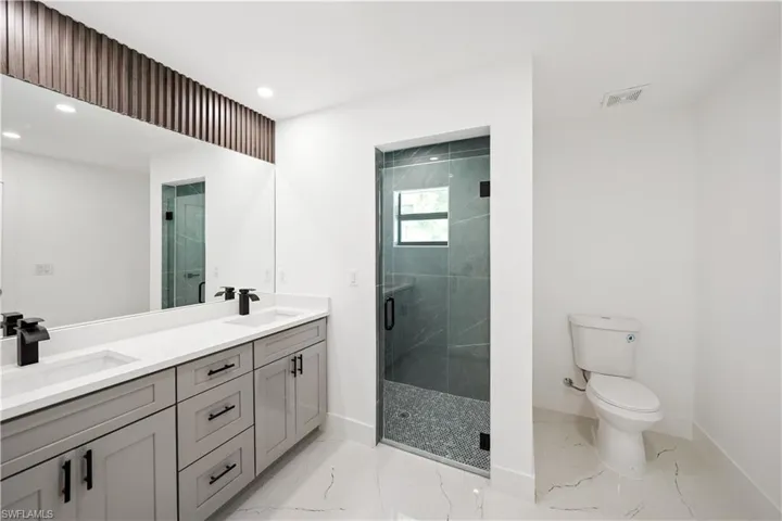 Bathroom featuring a double vanity with light gray cabinetry and black hardware, a large mirror, and a glass-enclosed shower with dark gray tile