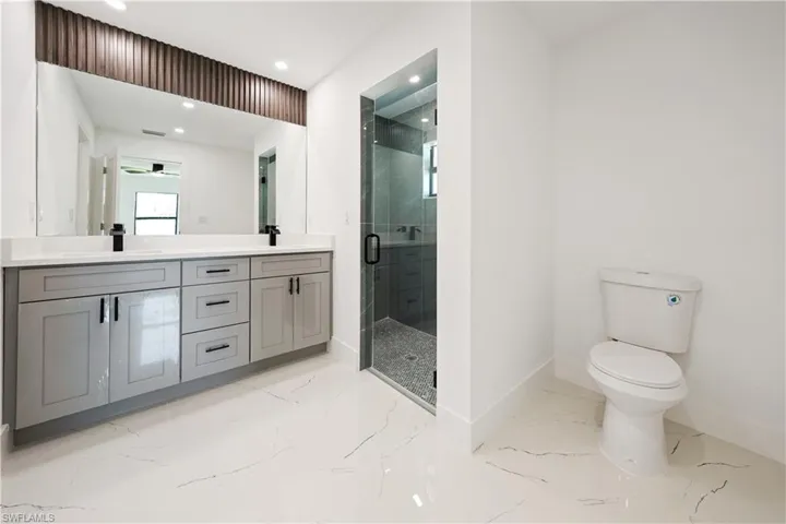 The bathroom features a double vanity with grey cabinetry, a large mirror, a glass-enclosed shower, and a toilet