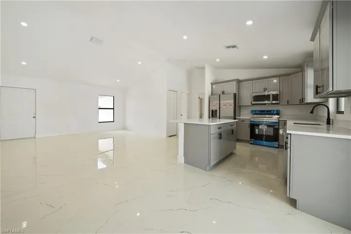 The property features an open-concept living space with polished tile flooring, recessed lighting, and a kitchen equipped with gray cabinetry, white countertops, and stainless steel appliances